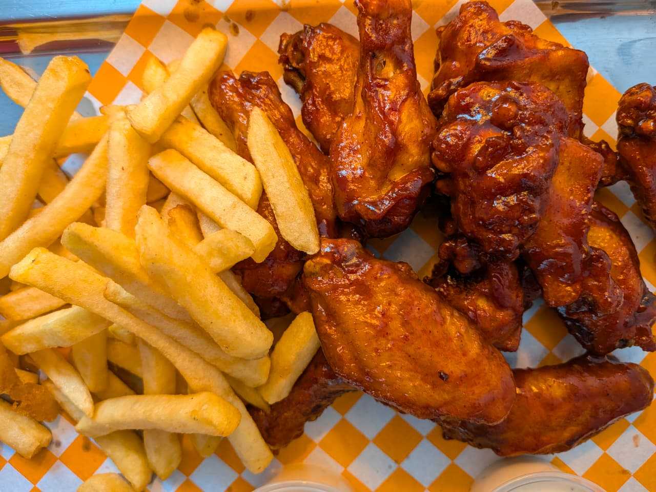 Alitas bañadas en salsa con papas a la francesa, sobre papel cuadriculado naranja